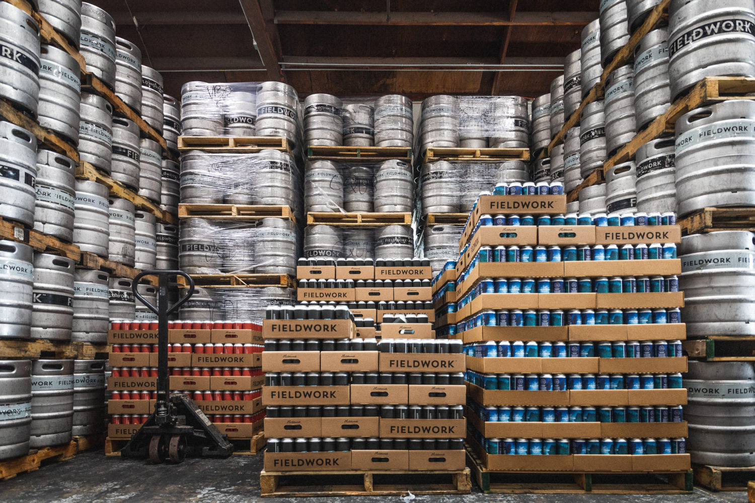 Fieldwork warehouse with an abundance of kegs and pallets of canned beer stacked high to the ceiling.